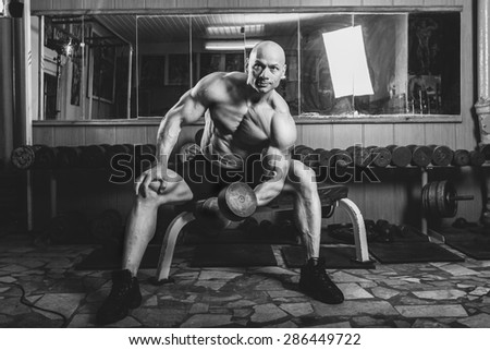 bodybuilder in the gym sitting on a bench and perform exercises.Black and white photo