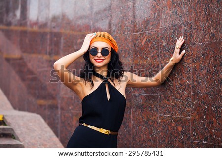 beautiful young girl in the orange hat and sunglasses walks down the street in the summer