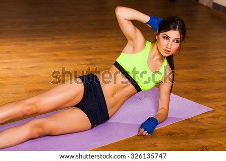 Young slender athletic girl on training in gym rocking abs while lying on the floor. dressed in a sports shirt and shorts, sneakers on his feet