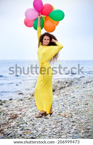 Beautiful girl in yellow long dress and long hair with balloons on the beach