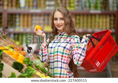 Young girl with red basket in hand selects fruits at the grocery store