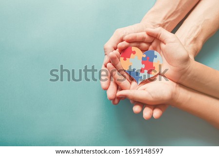 Adult and chiild hands holding jigsaw puzzle heart shape, Autism awareness, Autism spectrum disorder family support concept, World Autism Awareness Day