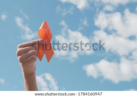 Hands holding orange Ribbon over blue sky,  Leukemia cancer and Multiple sclerosis, COPD and ADHD awareness, world kidney day 商業照片 © 