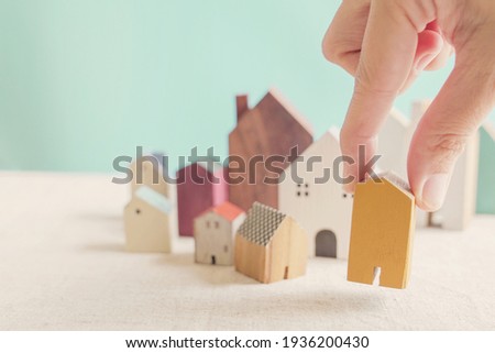 Hand choosing yellow miniature house, searching perfect property in high demand housing boom, choosing best house insurance, making right decision on home investment concept