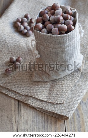 Hazelnuts in a cotton bag on a wooden table covered with burlap.