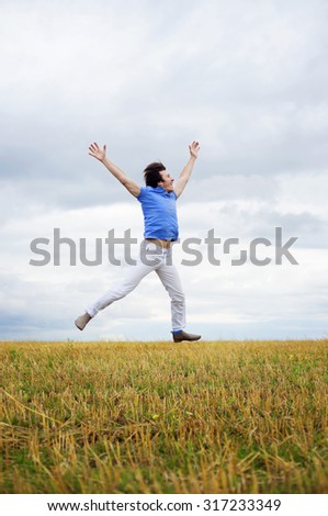 Man in a blue shirt jumping against cloudy sky