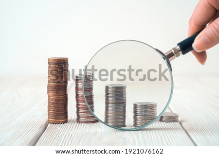 A hand with a magnifying glass examines the coins in stacks on a light background. Side view with copy space. The concept of finance, business, reduced income growth. ストックフォト © 