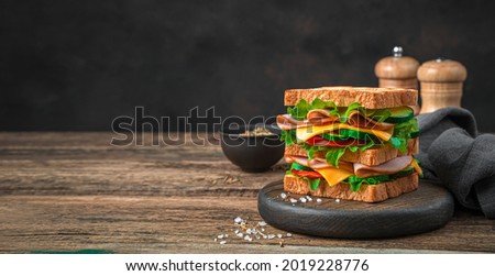 Delicious club sandwich with vegetables, ham, cheese and fried toast on a brown background. Side view, copy space.