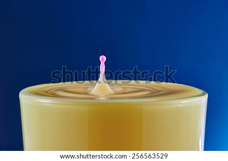 Pink drop splash in orange juice on blue background