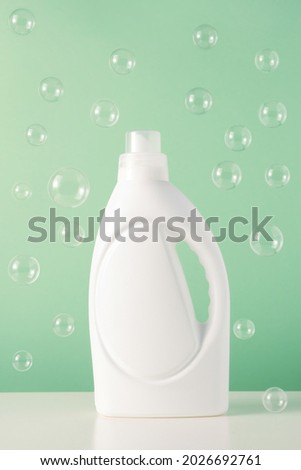 White plastic bottle of liquid laundry detergent or bleach or fabric softener with flying bubbles. Blank mockup packaging for cleaning agent on green background. Laundry day Foto stock © 