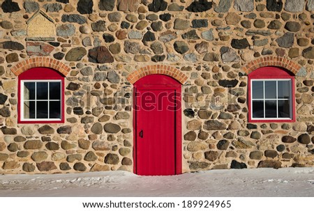 Old stone barn.  Photo taken in winter.  Warm sunlight.  Bright red door and window frames with brick arches.