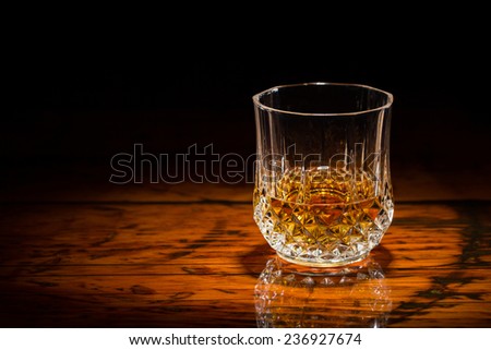 Whiskey and Wood - Liquor in a diamond-cut tumbler on a textured wooden table.  Spot light focused on the glass.  Copy space on left.  Upper frame fades to black.