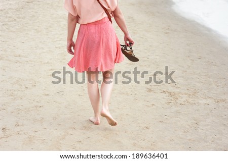 A young woman walking on the sand with flip-flops in hand