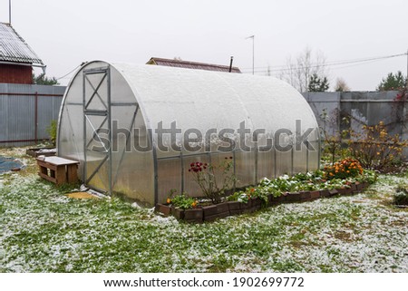 An empty polycarbonate greenhouse covered with the first snow in the garden in autumn