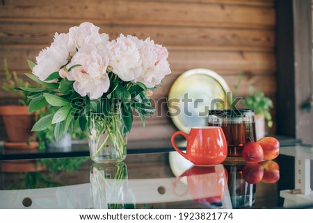Still life of tea accessories and flowers. Teapot with tea, tea mugs and a bouquet of peonies on a glass table on a bright day