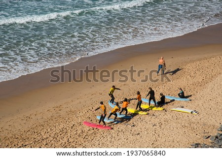 Beach landscape with active and sporty vacationers, such as bathers, swimmers and surfers. In a group and learning the skills in a surf school.