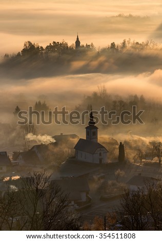 Église et villages se cachant au petit matin dans le brouillard. Un lever de soleil brumeux à la campagne.