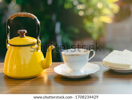 Yellow teapot on the wood table and white tea cup,Nature daylight and green garden,Afternoon rest time to relax from working at house,Home stay campaign to reduce the outbreak of the covid virus 2019.