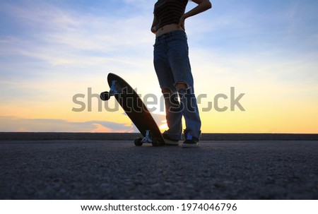 Portrait healthy young woman with lovely surf skate board on bridge along seashore aginst orange sky