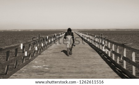 Man walking on a fishing pier, shot from behind. Sepia.