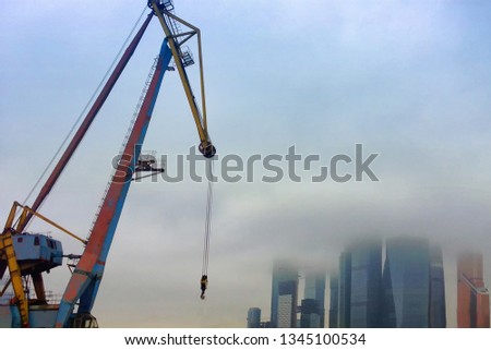 Construction of skyscrapers and high-rise buildings against a cloudy sky. The boom of a tower crane in the fog in Moscow-city