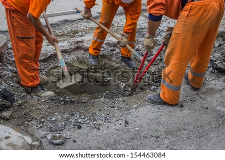 workers work on the replacement of cover slab with cast iron cover on the road with the help of a shovel and Bolt Cutter