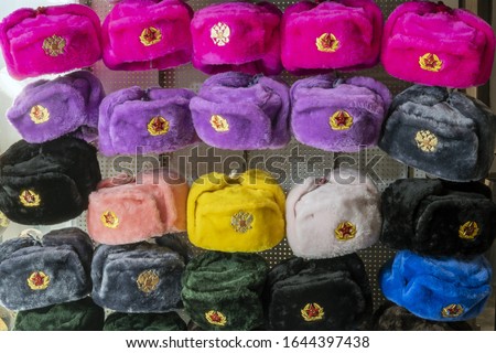 Military caps of different colors with the coats of arms of Russia and the USSR as Souvenirs from Moscow. Rows of russian winter hats of different colors with army emblems at the street market