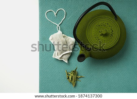 Lemon Verbena tea in teabag with heart shaped string  and teapot over a tidewater green background. Top View. Flat Lay