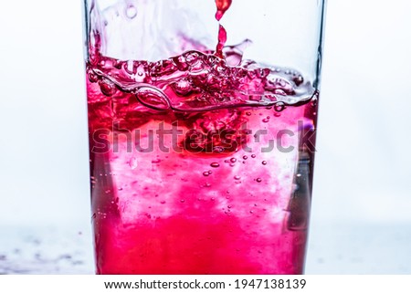 Líquido rojo vertido en un vaso. Fondo blanco.