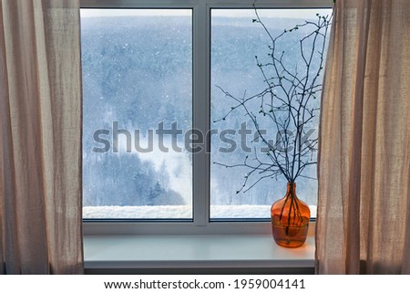 Branches of a tree with buds and blooming spring leaves stand in a vase at the winter window