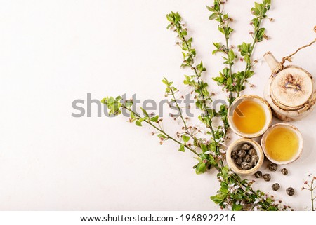 Branches of blossoming cherry tree with homemade ceramic teapot and green tea over white texture background. Top view, flat lay. Creative layout