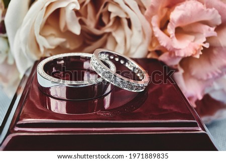 Closeup of white golden wedding rings on floral background. Bride ring with diamonds. Shallow focus. Love and wedding concept.