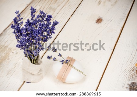 Exquisite natural soap garnished with twigs of lavender and a bunch of dried lavender in a canvas bag placed on vintage white wooden table