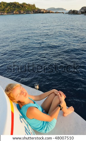 Thailand. Andaman sea. Similan islands. Calm blue sea, big stones and diving boat at a sunrise. Beautiful white-haired girl is taking a rest on the upper deck