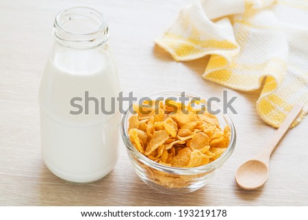 Bowl of cornflake and milk bottle on table