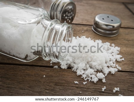 Spilled salt with salt shaker on wooden background