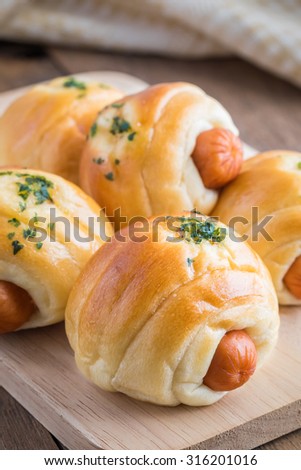 Bread roll with sausage on wooden plate