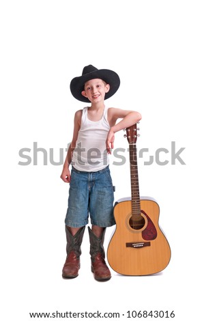 Cute young man with a cowboy hat and oversize boots leaning on an acoustic guitar. Isolated on a white background.