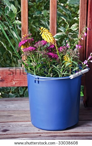 A mixture of spirea, red hot pokers, and other flowers in a bucket outside.