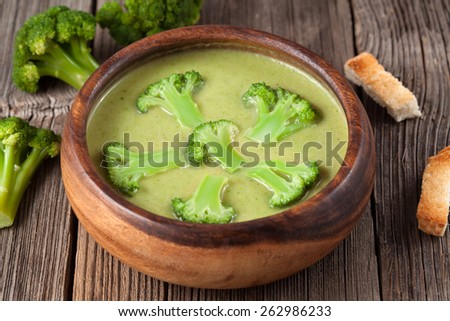 Gourmet cream of broccoli green soup in wooden bowl with croutons and fresh broccoli on background, on vintage table