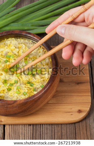 Unrecognizable man holding in hand food sticks with traditional egg drop soup in bowl on vintage wooden background