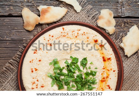 Plate of served hummus, traditional lebanese food with pita, paprika and parsley on vintage wooden background