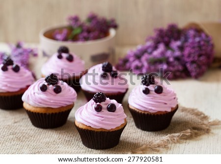 Homemade cupcakes traditional American sweet baked dessert with berries and lilac on vintage textile background. Natural light, rustic style.