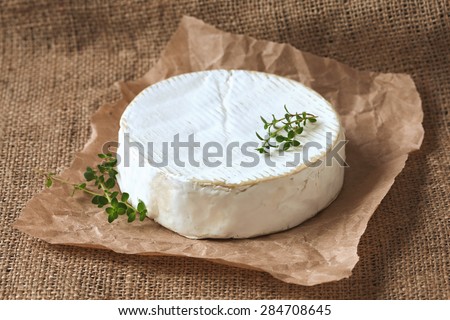 Camembert cheese delicious round french dairy food with fresh green thyme on rustic parchment. Rustic style, natural light. Vintage textile background.