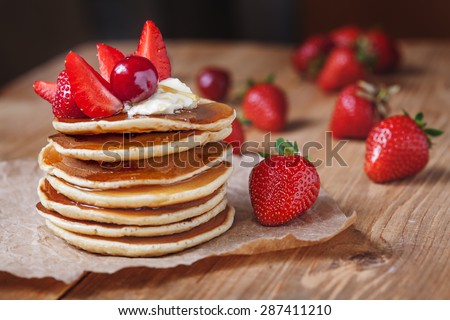 Homemade pancakes delicious breakfast or lunch dessert with strawberry, honey and butter on rustic kitchen table. Natural light rustic style.