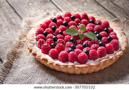 Delicious traditional homemade sweet raspberry tart cake dessert. Creamy pie with raspberries, whipped cream and mint on vintage rustic background. Rustic style and natural light.