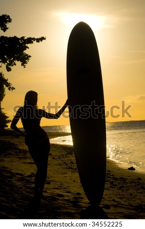 silhouette of a woman standing with a surfing board on the beach at sunset