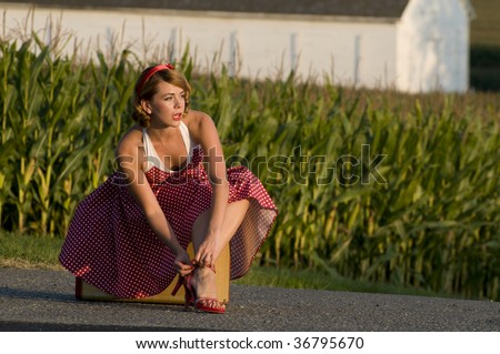 cute pinup girl fixing her sandal strap on the side of a country road