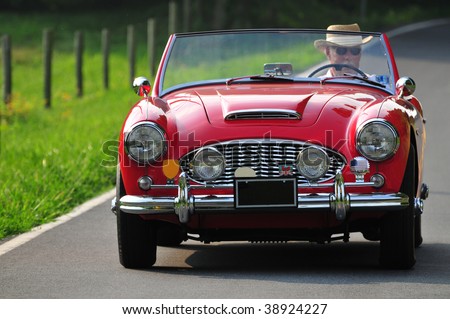 a senior man driving a classic red sports car on a country road