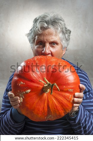 Halloween theme. Closeup of an old woman eating a big orange pumpkin freshly harvest in autumn. Studio shoot and color image.